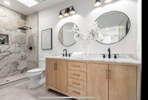 A newly remodeled bathroom featuring a double vanity, round mirrors, and a walk-in shower with marble-look tiles by American Wolf Construction in Mesa, AZ