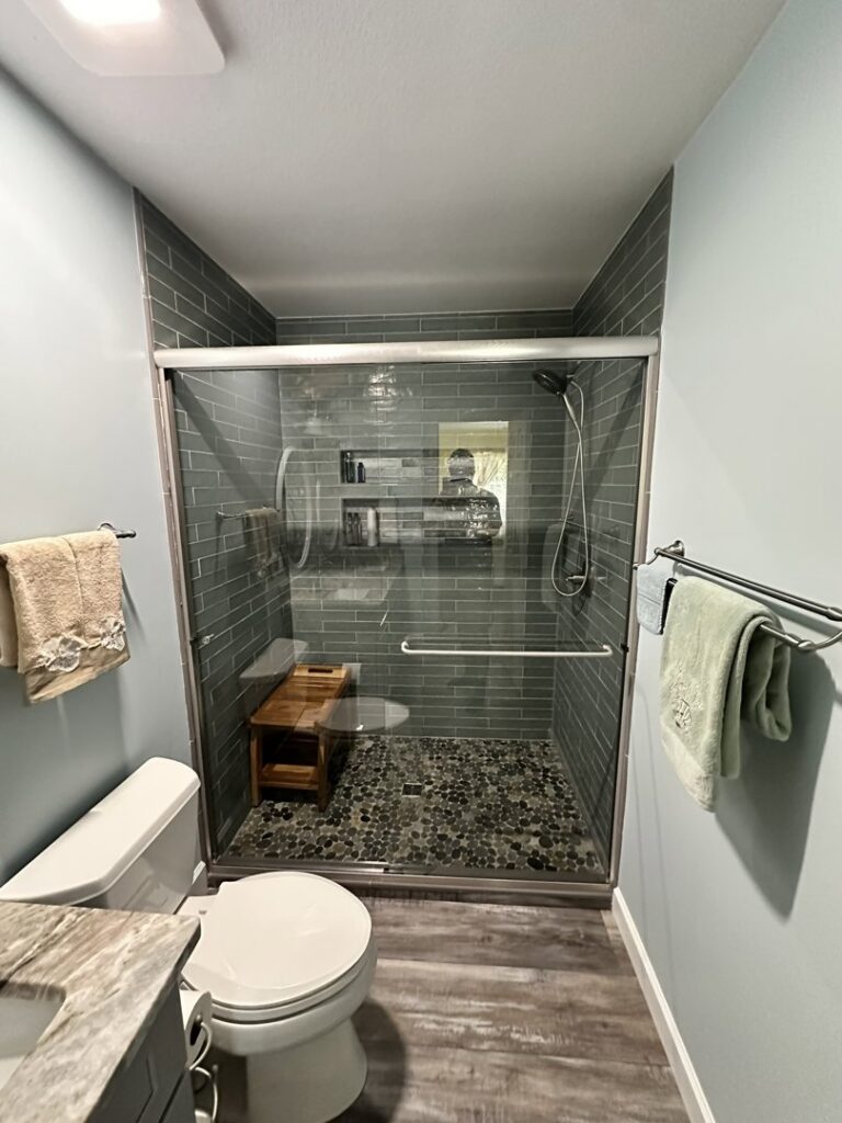 A newly remodeled bathroom featuring a glass shower enclosure with green subway tiles by Four Seasons Building & Remodeling in Mauldin, SC.