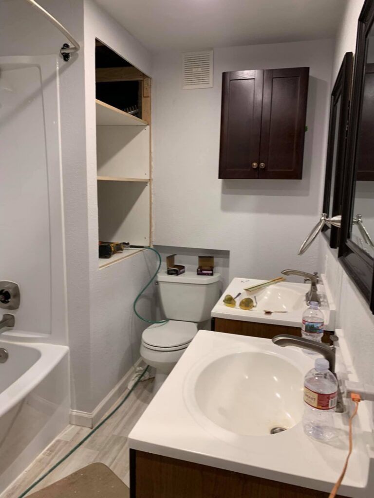 A bathroom undergoing renovation, featuring new sinks, toilet, and shelving installation by Vazquez Quality Construction Inc in Aurora, CO.
