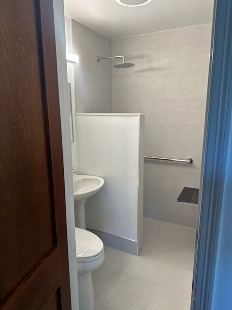 A remodeled small bathroom featuring a pedestal sink and accessible shower by Dynamic Design & Remodeling in Westport, CT