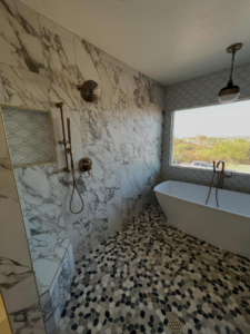 A modern bathroom remodel featuring a tiled shower, freestanding tub, and pebble floor by Raven Construction LLC in Tucson, AZ.