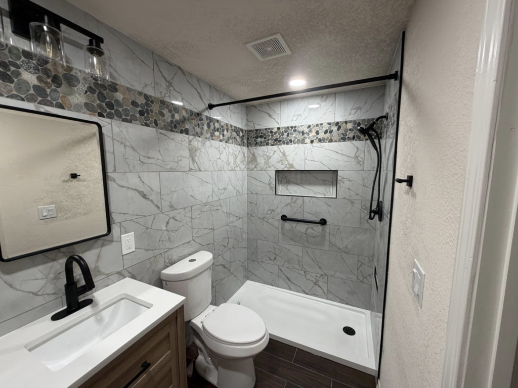 A newly remodeled bathroom featuring a tiled shower, new vanity, and toilet by RK Pro Service Inc in Colorado Springs, CO.