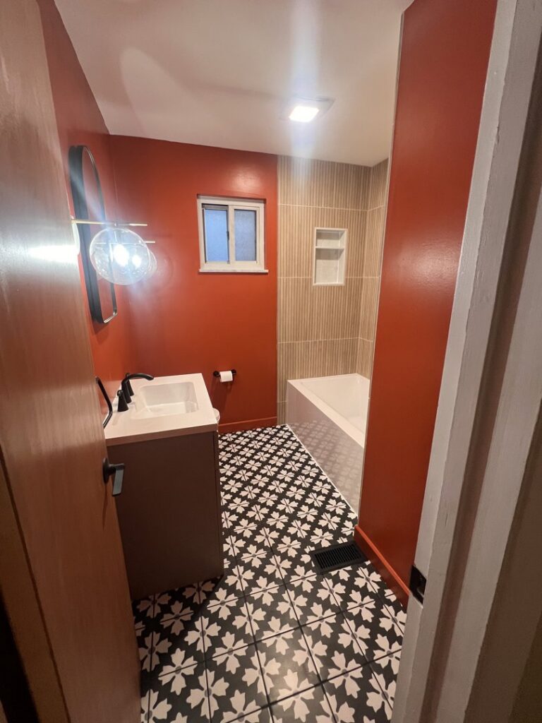 A newly remodeled bathroom featuring a modern vanity, patterned floor tiles, and orange walls by Gold-Mine Construction, LLC in Pittsburgh, PA.