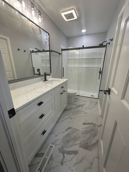 A modern bathroom remodel with a white vanity, black fixtures, and a sliding glass shower door by Benjamin Design - Build in Fishers, IN.