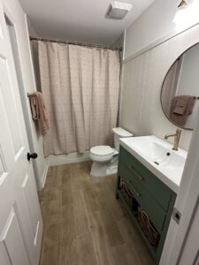 A bathroom remodel featuring a green vanity, wood-look tile floor, and a shower/tub combo by CMT Construction LLC in Columbia, MO.