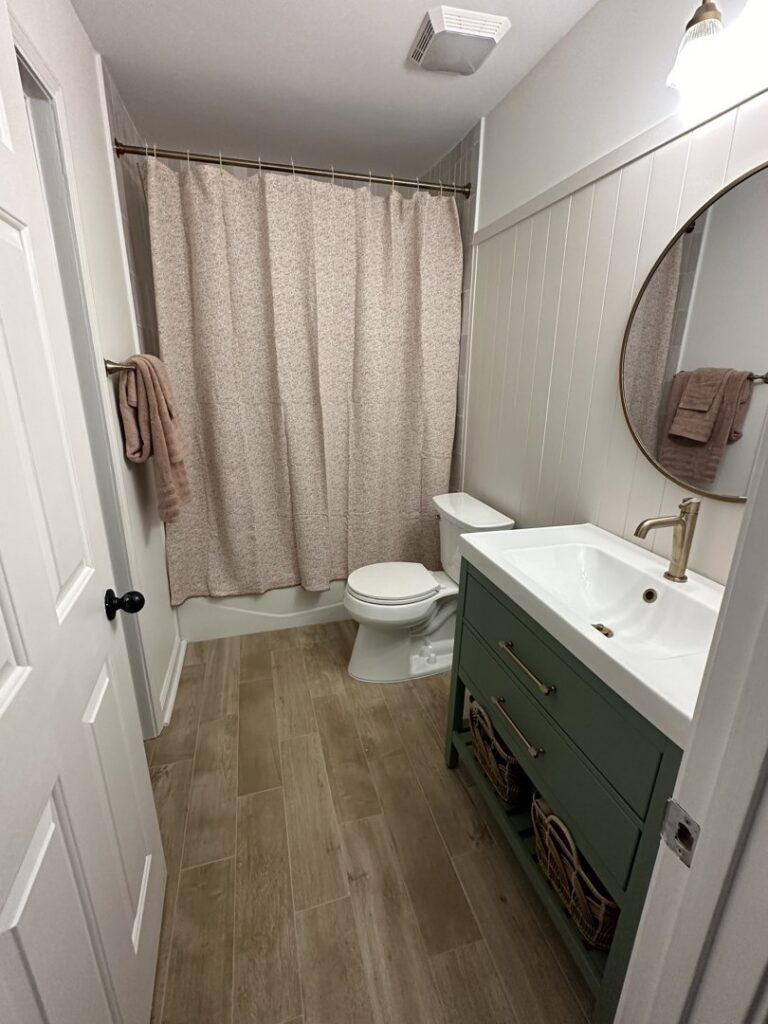 A bathroom remodel featuring a green vanity, wood-look tile floor, and a shower/tub combo by CMT Construction LLC in Columbia, MO.