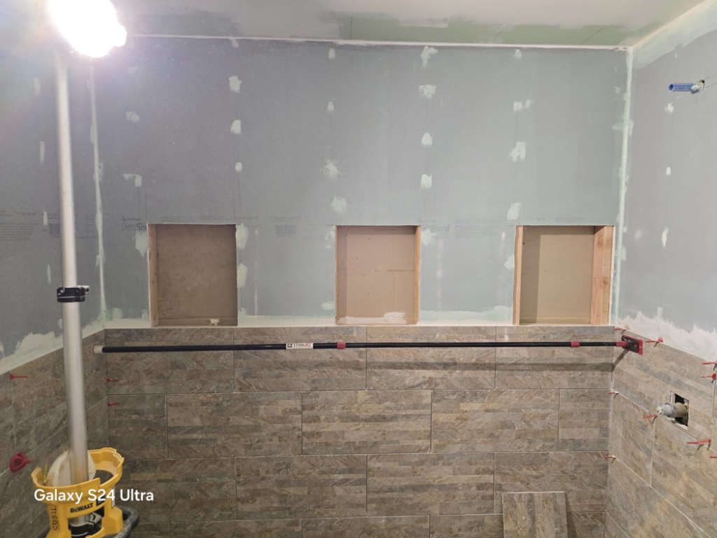 Bathroom remodel work in progress, showing framed shower niches, partial tiling, and a work light by Torres Services in Anchorage, AK.