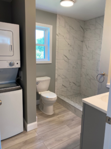 A modern renovated bathroom with a tiled walk-in shower and stacked laundry by Casco Bay Construction Services, LLC in South Portland, ME.