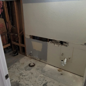 A bathroom in the demolition phase of a renovation project by Tier 1 Contracting Inc. in Apache Junction, AZ, showing exposed studs and plumbing.