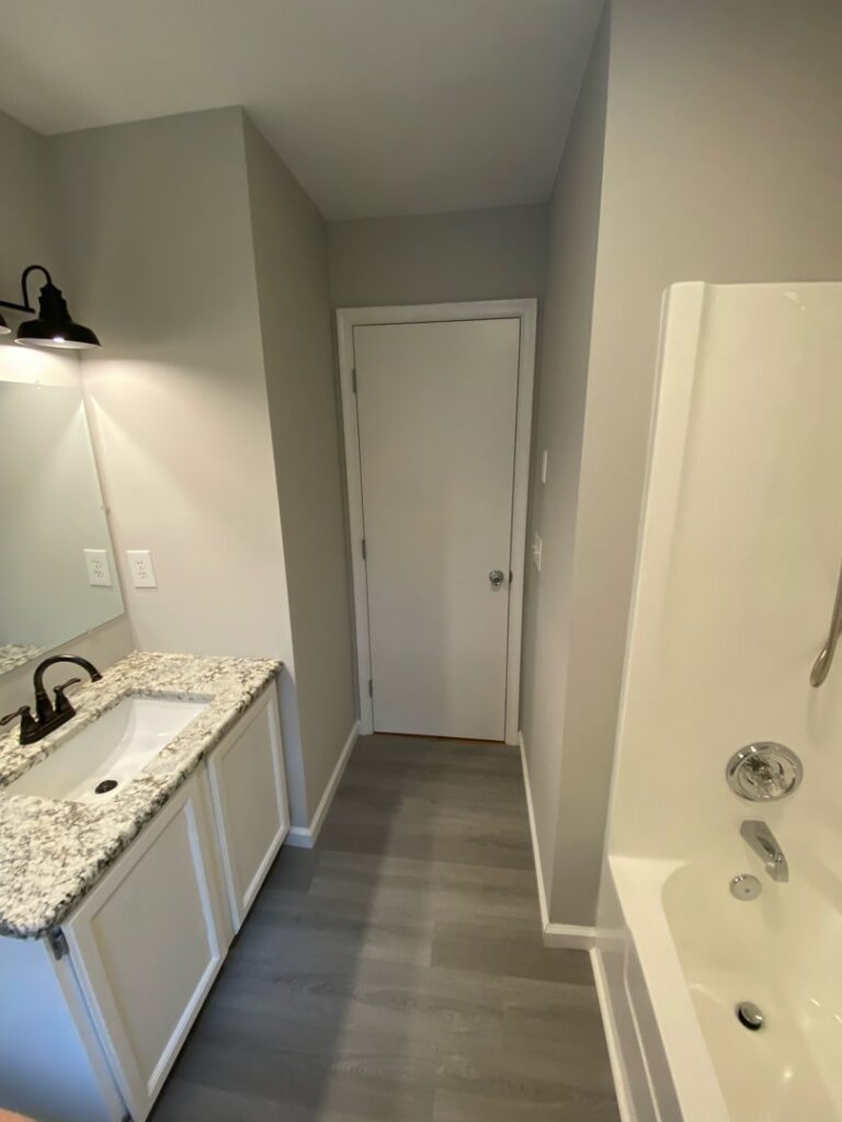A newly renovated bathroom featuring a white vanity with granite countertop, sink, and bathtub by Shore Home Construction Roofing in Salisbury, MD.