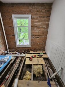 A bathroom renovation in progress showing exposed brick, subfloor, and plumbing work by Imperial Access Contracting in Evansville, IN.