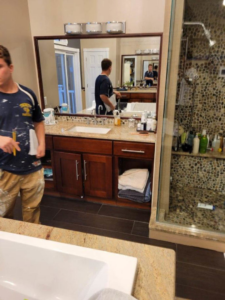 A bathroom renovation in progress, showing a vanity, mirror, and pebble-tiled shower by Infinite Construction LLC in Bristol, CT.