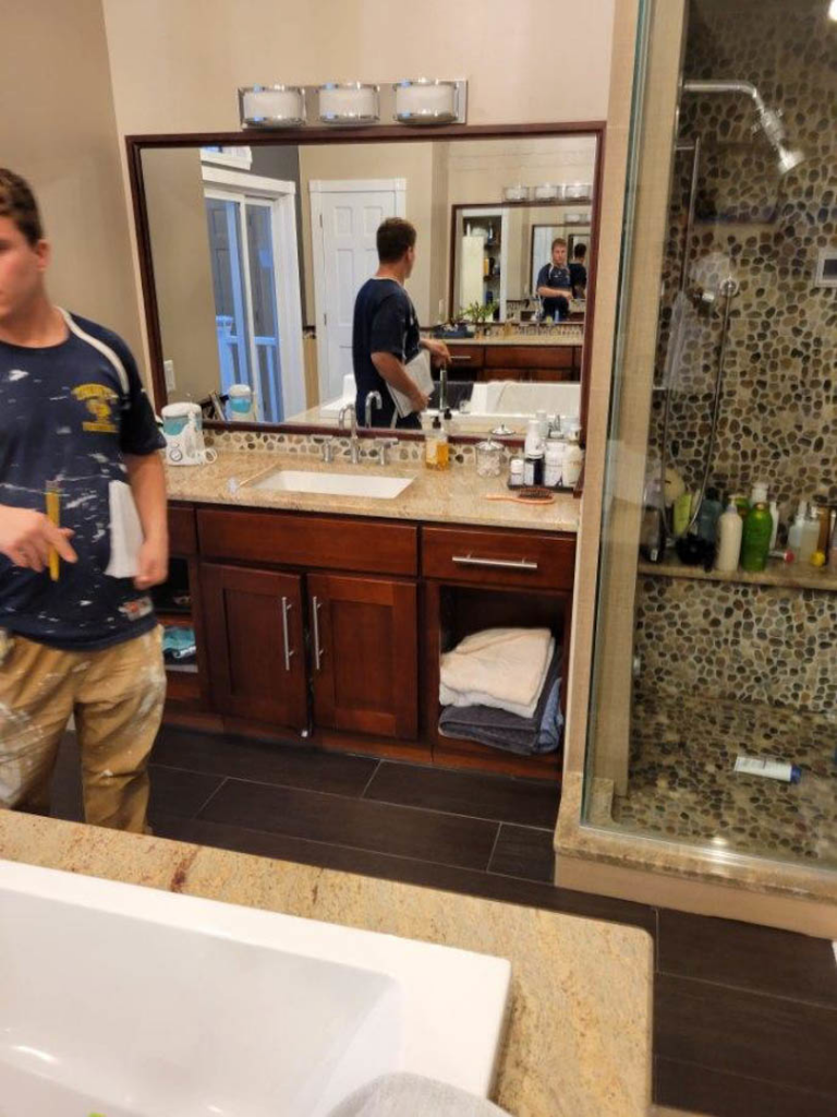 A bathroom renovation in progress, showing a vanity, mirror, and pebble-tiled shower by Infinite Construction LLC in Bristol, CT.