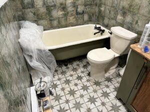 A bathroom renovation in progress, showing a covered bathtub, new toilet, and patterned floor tiles by Tile Jawn in Philadelphia, PA.