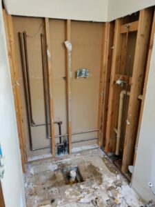 A bathroom under renovation with walls stripped to studs, exposing plumbing pipes, demonstrating a handyman's work by Homefix Lawrence in Lawrence, KS.