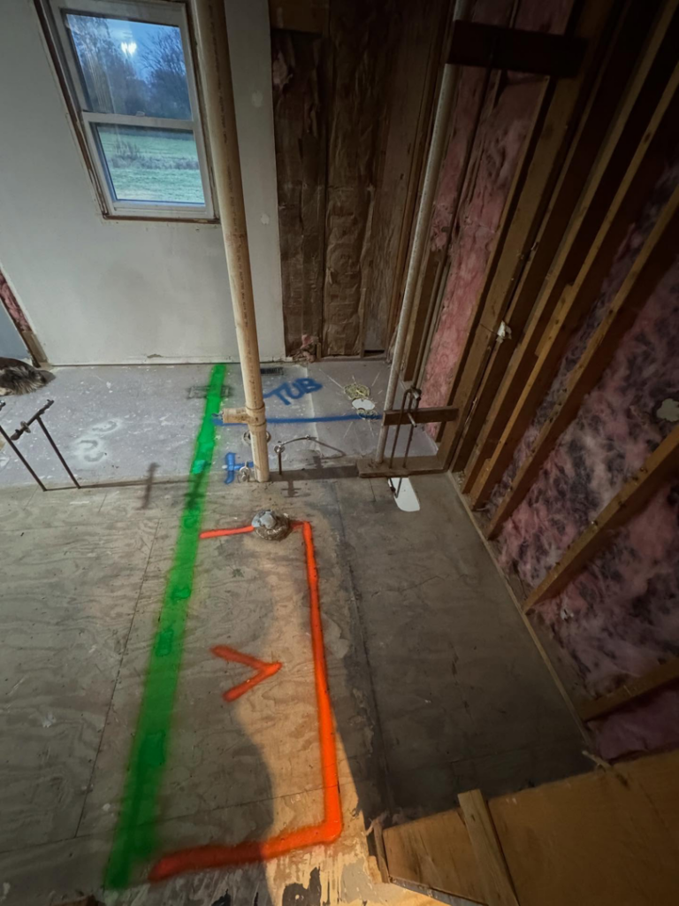 A bathroom renovation in progress, showing exposed plumbing, insulation, and floor markings for a new tub layout by Shackelford Home Designs in Loveland, OH.