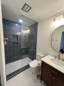 A newly renovated bathroom featuring a walk-in shower with dark blue subway tiles, a modern toilet, and vanity, by Boyd's Custom Building in Charlotte, NC.