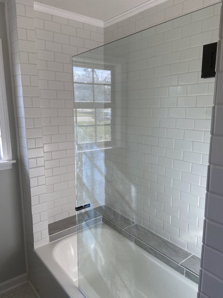 A renovated bathroom featuring new white subway tiles and a glass shower screen over a bathtub, completed by Lee's Handyman Service LLC in Oxford, MS.