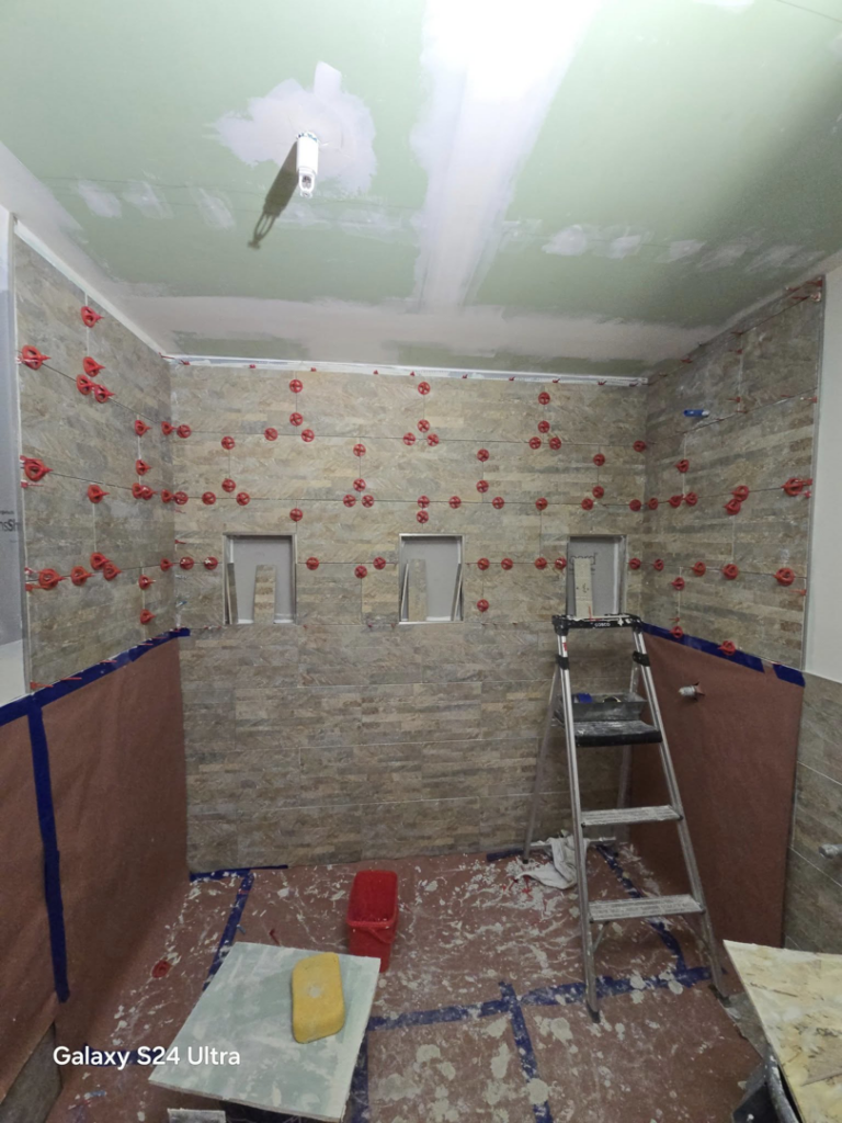 A bathroom renovation project in the tiling stage, with spacers on the walls and a ladder, by Torres Services in Anchorage, AK.