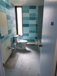 Bathroom renovation showing blue tiles, a toilet, and minor debris by Green Man's Contracting & Landscaping LLC in West Hartford, CT.