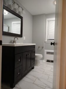 A renovated bathroom featuring a dark vanity, large mirror, and white marble-look tile flooring by Brothers Home Improvement in East Hartford, CT