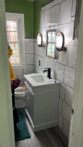 A bathroom undergoing renovation, featuring new wall tiles, a white vanity, and modern light fixtures by J&A Contractor LLC in Milwaukee, WI.