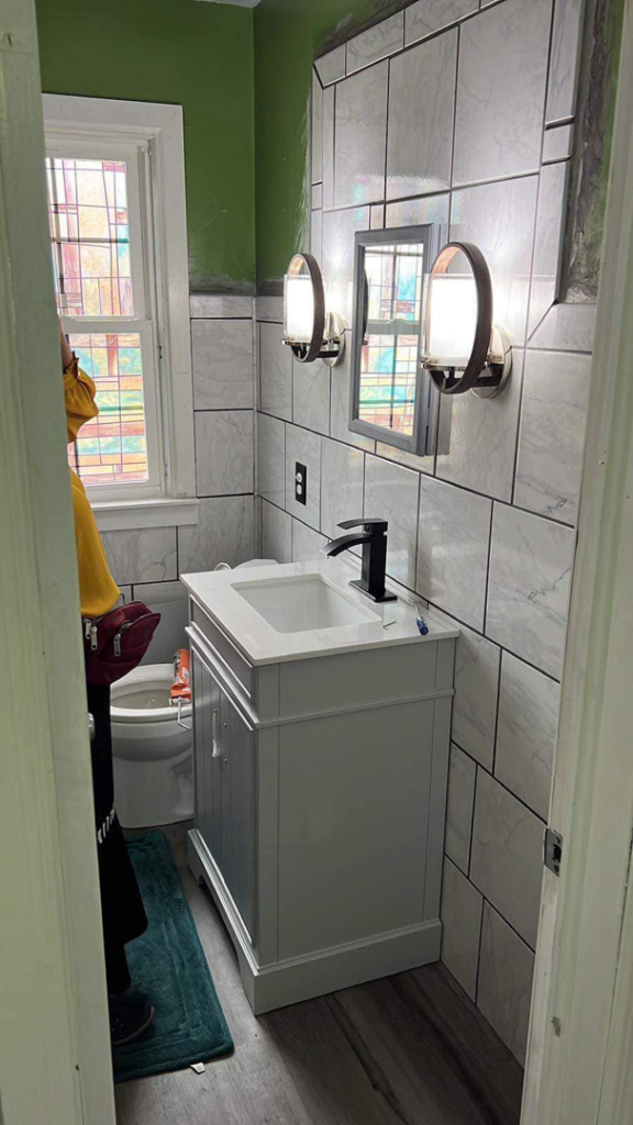 A bathroom undergoing renovation, featuring new wall tiles, a white vanity, and modern light fixtures by J&A Contractor LLC in Milwaukee, WI.