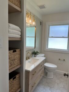 A renovated bathroom showcasing a wood vanity, toilet, and practical open shelving with baskets by Westrick Homes in St. Louis, MO.