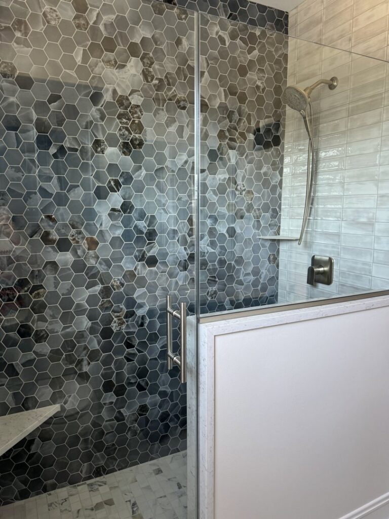 A modern bathroom shower featuring stylish hexagonal grey tiles and a clear glass door by Synergy Builders in West Chicago, IL.