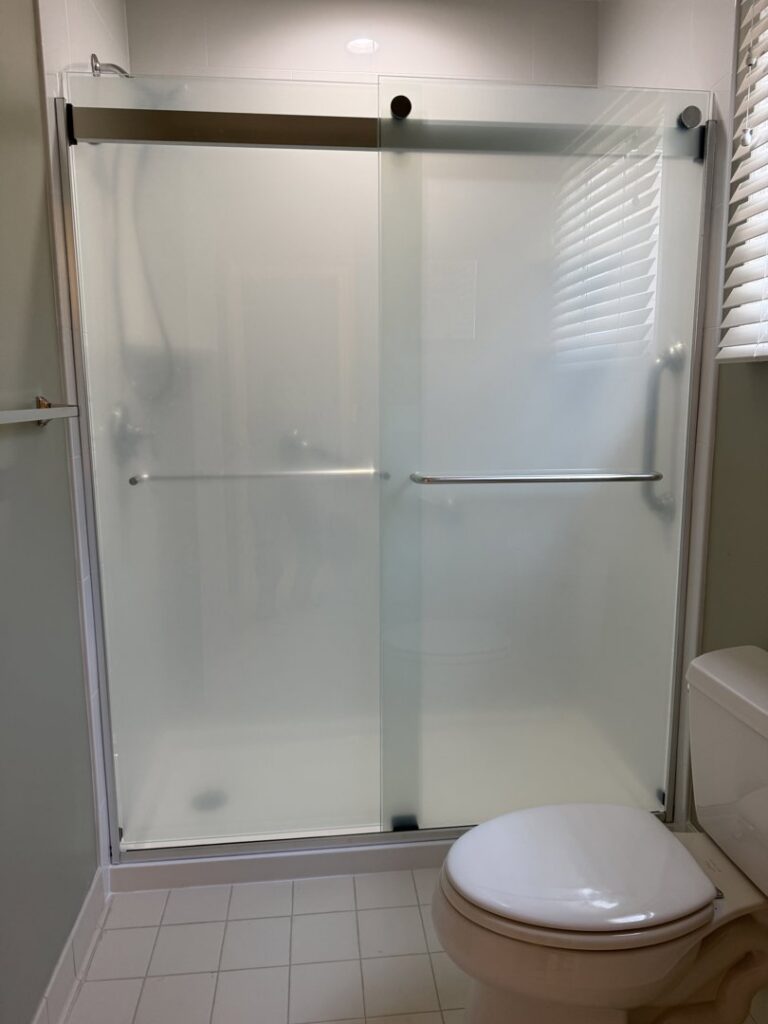 A bathroom featuring a newly installed shower with a frosted glass sliding door by Peninsula Bath & Tile in Salisbury, MD.