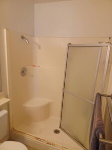 An old and worn shower stall with a misaligned glass door, representing a bathroom renovation project by Integrity Management in San Diego, CA.