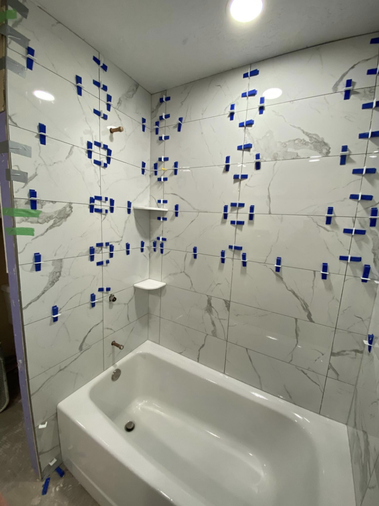 Bathroom shower tile installation in progress with white marble-look tiles by Cutting Edge Carpentry & Construction in Lawton, OK.