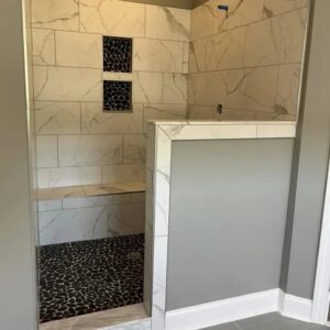 Bathroom shower with marble-look wall tiles and black pebble floor installed by Santizo Flooring & Painting in Raleigh, NC.