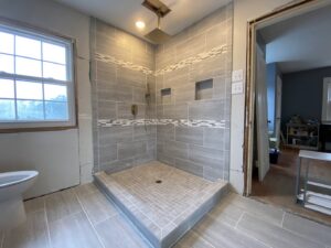 A bathroom shower tiling project in progress with grey tiles and an accent strip by Goubar Tile And More in Raleigh, NC.