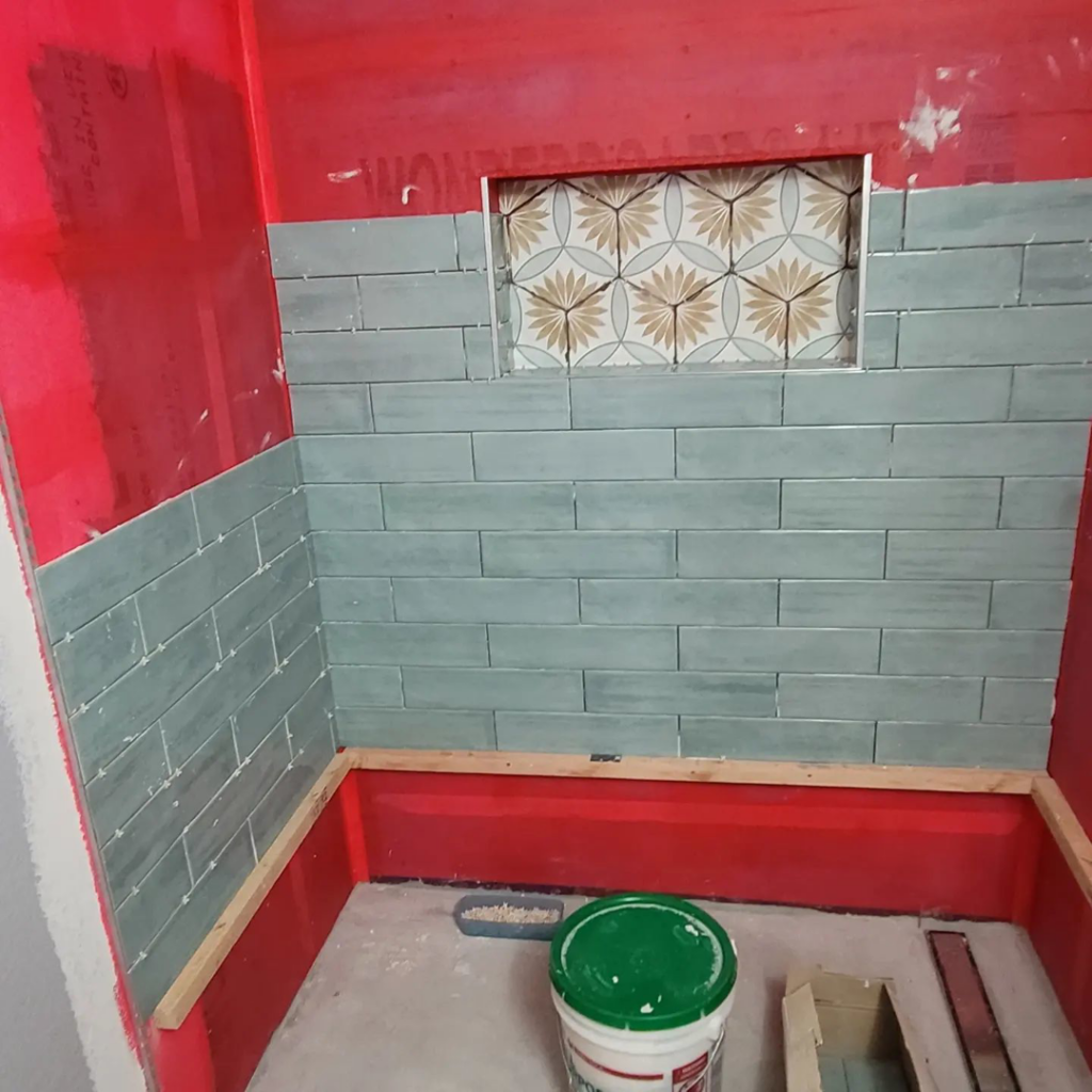 Shower tiling in progress with blue-green subway tiles and decorative niche tiles by Tier 1 Contracting Inc. in Apache Junction, AZ.
