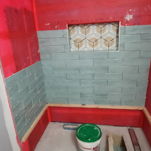 Shower tiling in progress with blue-green subway tiles and decorative niche tiles by Tier 1 Contracting Inc. in Apache Junction, AZ.