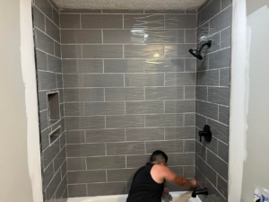 A person installing grey subway tiles in a shower and bathtub area, a service provided by JB Recovery in Columbus, OH.