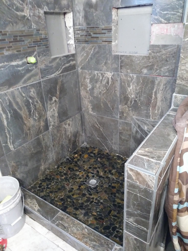 An unfinished bathroom shower with dark tile walls and a pebble stone floor installed by Barrios Remodeling in Kansas City, MO.