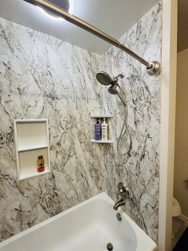 A renovated bathroom shower and tub with marble-patterned wall panels by APS Residential Services in Livonia, MI.