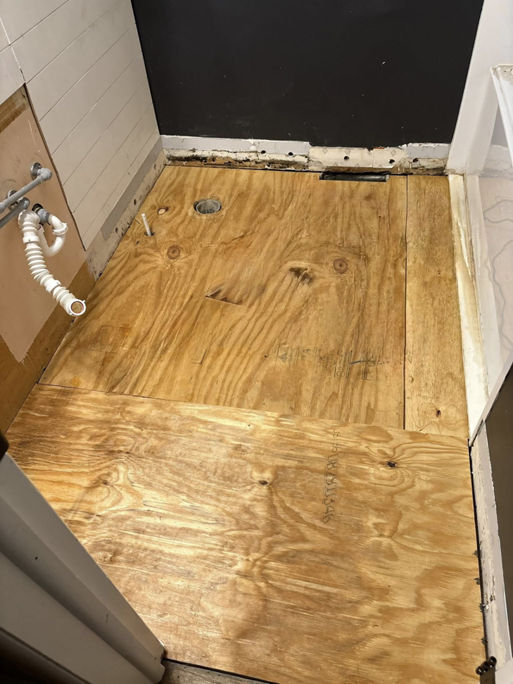 A bathroom subfloor with exposed plumbing pipes, ready for new flooring installation by CJ Flooring LLC in Flat Rock, MI.