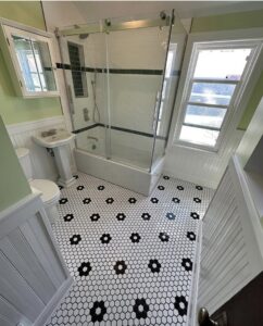A renovated bathroom with a shower-tub combo, glass enclosure, and decorative black and white floor tiles, completed by Orion Construction Services in Duluth, MN.