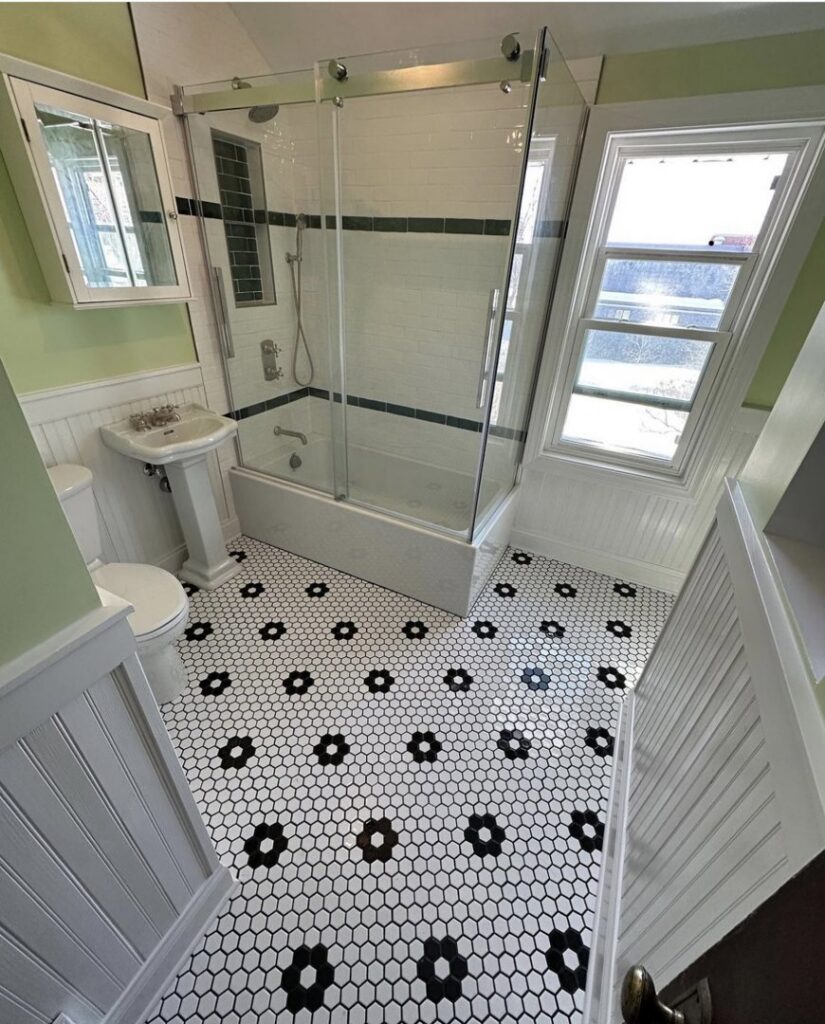 A renovated bathroom with a shower-tub combo, glass enclosure, and decorative black and white floor tiles, completed by Orion Construction Services in Duluth, MN.