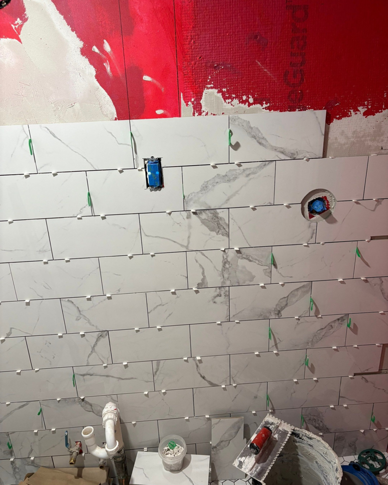 Marble-patterned tiles being installed on a bathroom wall by Clearview Home Remodeling in Parkville, MD.