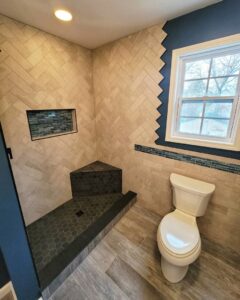 Renovated bathroom with a tiled shower featuring a herringbone pattern, a corner bench, and a toilet by Supreme Tile & Flooring in Charlotte, NC.
