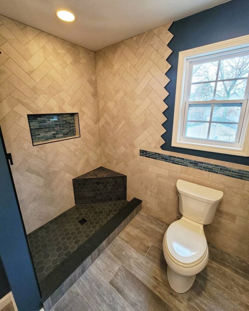 Renovated bathroom with a tiled shower featuring a herringbone pattern, a corner bench, and a toilet by Supreme Tile & Flooring in Charlotte, NC.