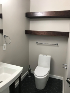 A newly installed toilet, sink, and floating shelves in a modern bathroom by Kaya Construction in Portland, OR.