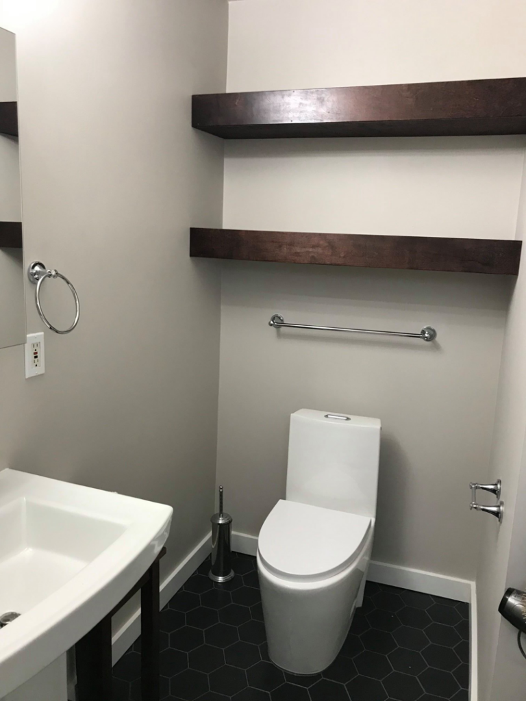 A newly installed toilet, sink, and floating shelves in a modern bathroom by Kaya Construction in Portland, OR.