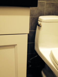 A newly installed toilet next to a white vanity with dark tiled walls in a bathroom by Executech Interiors in Yonkers, NY