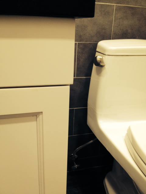 A newly installed toilet next to a white vanity with dark tiled walls in a bathroom by Executech Interiors in Yonkers, NY