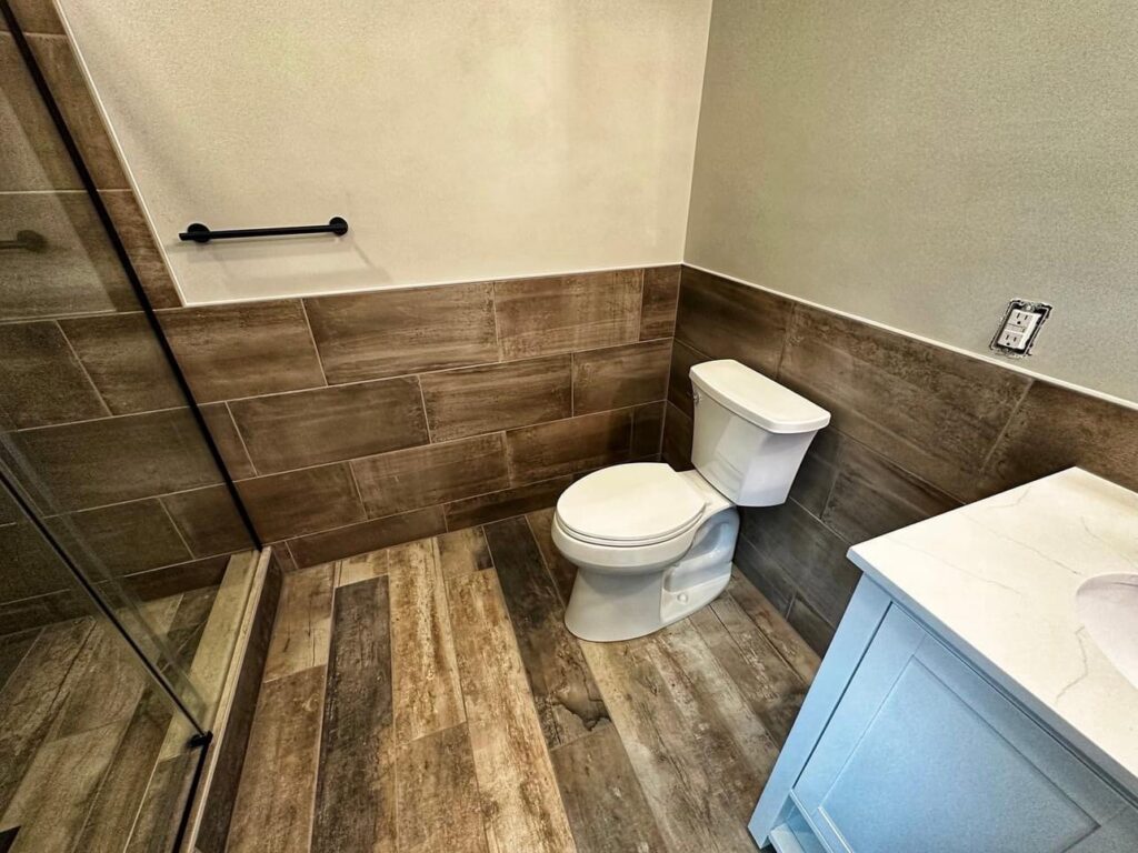 Bathroom with a toilet and wood-look tiles installed on the floor and lower walls by Supreme Tile & Flooring in Charlotte, NC.